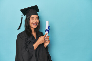 Celebrating Filipina graduate with diploma and cap on blue studio