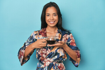Filipina in floral kimono enjoying a tea moment on blue studio backdrop