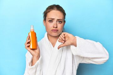 Blonde in bathrobe with sunscreen cream in studio showing a dislike gesture, thumbs down....