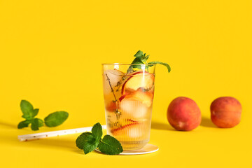 Glass of fresh peach lemonade with mint and fruits on yellow background