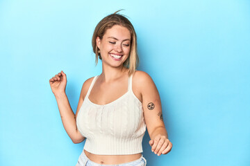 Blonde young woman in white top on blue background dancing and having fun.
