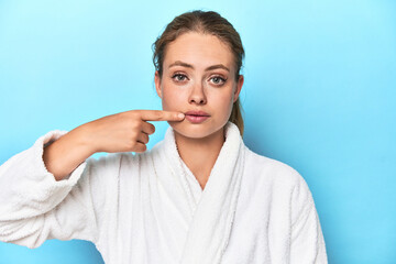 Young blonde woman in a white robe posing seriously in a studio