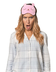 Blonde in pajamas with sleep mask shouting very angry, rage concept, frustrated.