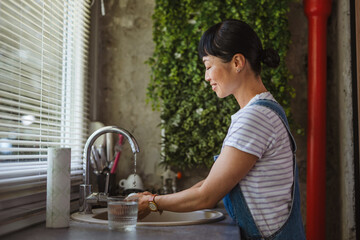 happy mature japanese woman wiping drinking glass at home kitchen
