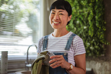 happy mature japanese woman wiping drinking glass at home kitchen
