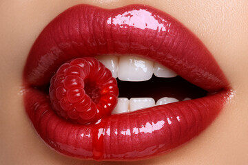 Glossy red lips holding a raspberry
