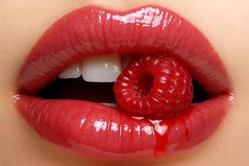 Glossy red lips holding a raspberry