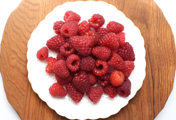 Ripe red raspberries on a blue plate on a wooden background. Sweet raspberry background. Berries close-up. Healthy food.