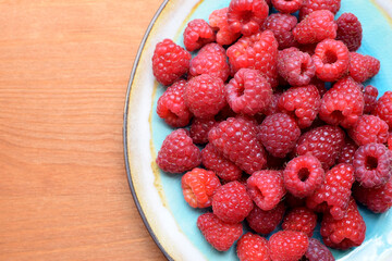 Ripe red raspberries on a blue plate on a wooden background. Sweet raspberry background. Berries close-up. Healthy food.