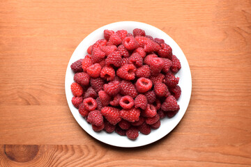 Ripe red raspberries on a white plate on a wooden background. Sweet raspberry background. Berries close-up. Healthy food.