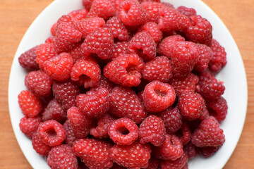 Ripe red raspberries on a white plate. Sweet raspberry background. Berries close-up. Healthy food