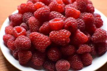 Ripe red raspberries on a white plate. Sweet raspberry background. Berries close-up. Healthy food
