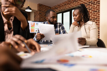 Black business team evaluating company documents, seated in office, collaborating on project presentation during meeting. African american male and female professionals analyzing financial paperwork.