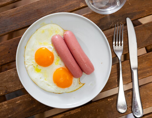 There is freshly cooked breakfast on plate - scrambled eggs with whole of fried pork chicken sausage. Traditional European Spanish breakfast is fried eggs with sausage