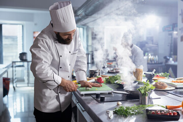 Young male head chef making crushed garlic on the cutting board, pressing the cloves to use...