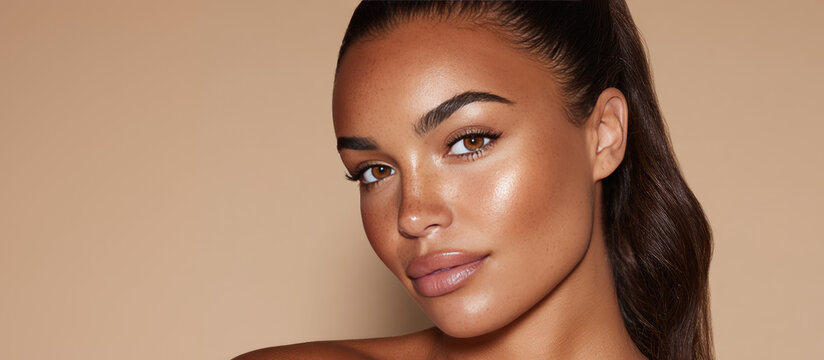 A woman with glowing skin and long dark hair looks towards the camera, displaying a natural makeup look. Beauty and skincare portrait