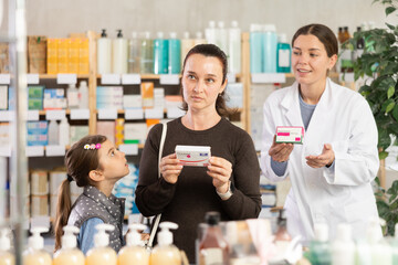 Selective middle-aged woman with daughter choosing paracetamol and female pharmacist offering medicine in chemistry