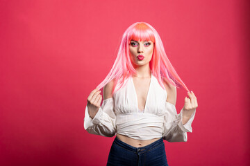 Confident woman in pink wig and off shoulder top poses with playful pout while holding strands of...
