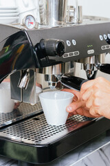 Barista hands operating espresso machine with coffee cup