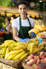 Positive female seller offers to buy ripe tasty bananas in grocery department of the supermarket
