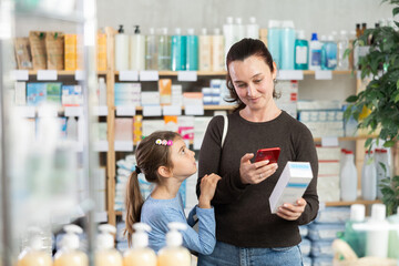 Woman and girl daughter in pharmacy scans QR code on cream and uses link to go to manufacturers...