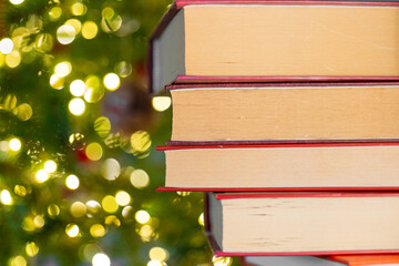 Books with red covers stack on Christmas tree background. Books on the shelf and fir branches with...