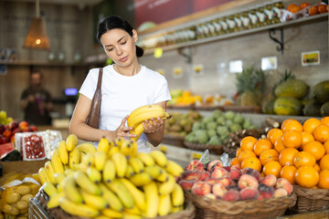 Adult woman buyer choosing bunch of fresh bananas in vegetable shop