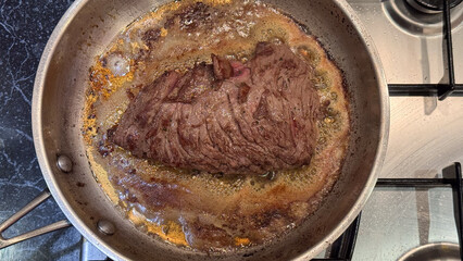 Top-down view of a beef steak searing in a stainless steel pan on a stove
