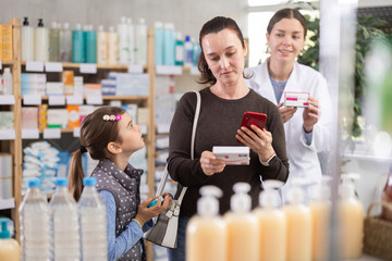 Woman with a child stands near a medicine counter and scans the barcode of a package of pills in front of 