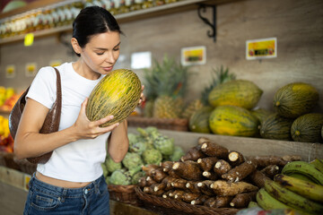 Woman choosing ripe tasty melon in grocery department of supermarket