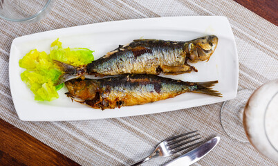 Two appetizing fried sardines with lettuce leaves. Close-up image..