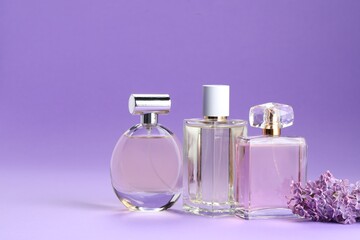 Bottles with perfumes and lilac flowers on purple gradient background, closeup. Space for text