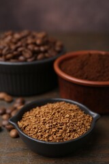 Different types of instant coffee and beans in bowls on wooden table against brown background, closeup