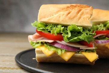 Pieces of tasty baguette sandwich with ham, cheese and vegetables on wooden table against grey background, closeup
