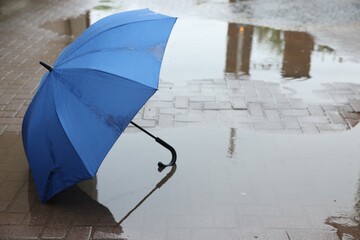 Blue umbrella on wet asphalt outdoors, space for text