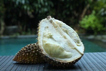 Fresh ripe durian on wicker table near swimming pool outdoors, closeup