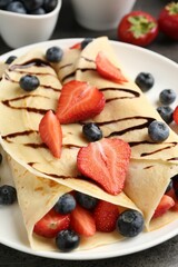Tasty crepes with strawberries, blueberries and chocolate sauce on table, closeup