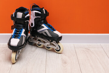Pair of roller skates on floor near orange wall, space for text