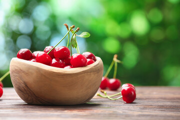 Fresh wet cherries in bowl on wooden table against blurred green background, closeup