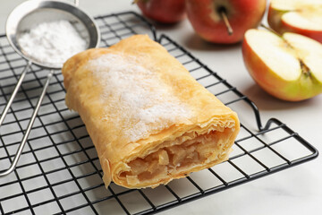 Tasty apple strudel with powdered sugar and fruits on white marble table, closeup