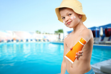 Little boy with tube of sunscreen by outdoor swimming pool. Sun protection product on his skin