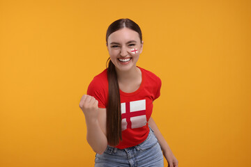 Excited fan with flags of England on her face and t-shirt against orange background