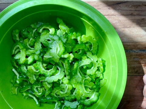 several raw slices of bitter melon vegetables in a green bowl on a wooden table ready to be cooked into a healthy meal - Powered by Adobe