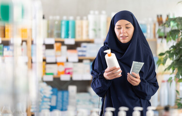 Uncertain young female customer trying to choose cream in chemist's shop