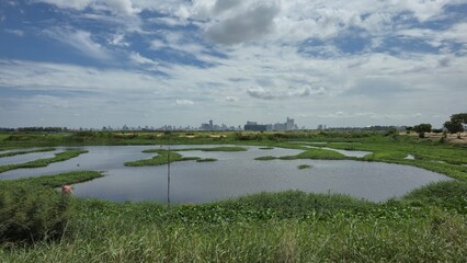 Outskirts of Phnom Penh, Cambodia – 25 June 2025. A wetland pond with green patches stretches...