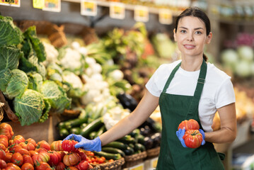 Girl puts ripe tomato in box on display case, arranges assortment in vegetable shop. Worker puts...