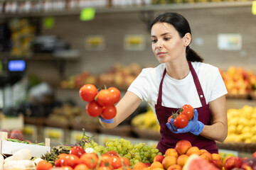 Shop seller put goods on display case. Girl creates stock of tomato in display case, forms...