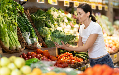 Adult woman buyer choosing fresh cabbage in vegetable shop