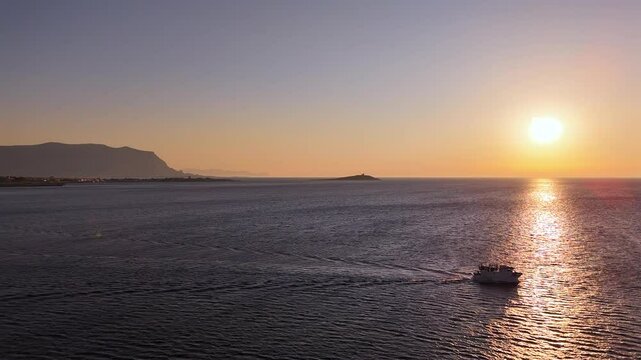 Peschereccio in navigazione nel golfo di sferracavallo accarezzato dal sole al tramonto durante una battuta di pesca estiva al gambero rosso di mazzara del vallo vista dall'alto con drone
