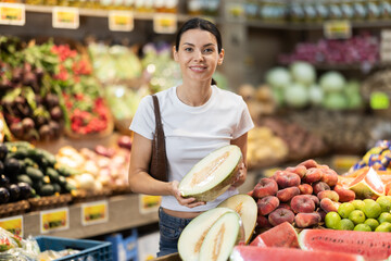 Woman choosing ripe tasty melon in grocery department of supermarket